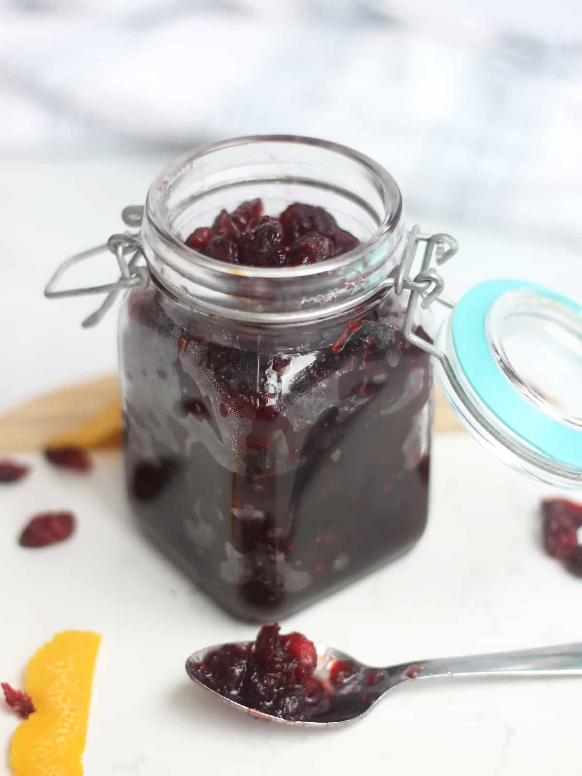 A jar of dried cranberry sauce with some on a teaspoon next to it.