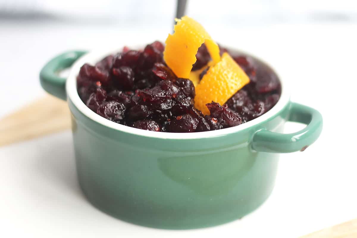 Cranberry sauce served in a green pot with curled orange peel.