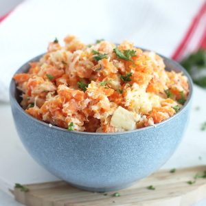 Mashed carrots and parsnips in a blue bowl with fresh herb garnish.