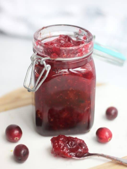 Whiskey cranberry sauce in a jar next to a spoon with some of the sauce on it.