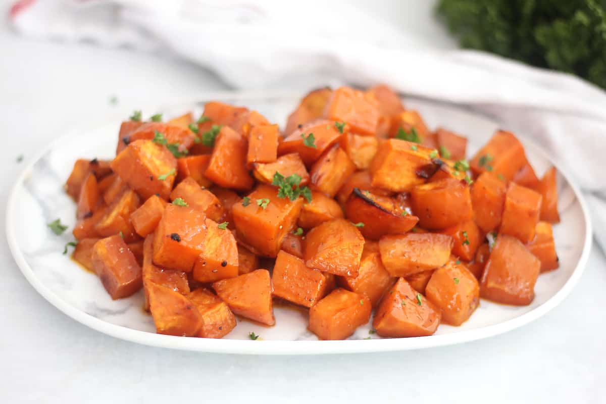 Roasted sweet potatoes on a white swerving plate garnished with parsley.