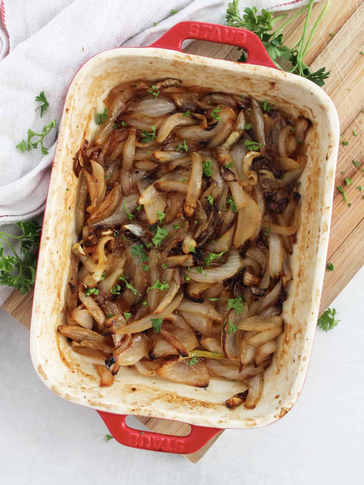 Caramelized onions in a red baking dish garnished with fresh parsley.