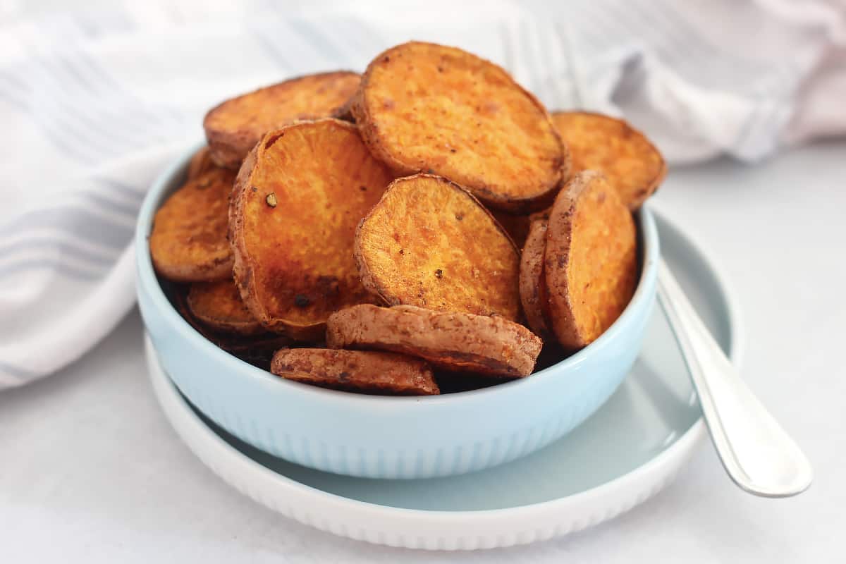 Baked sweet potato slices in a blue bowl with a fork.