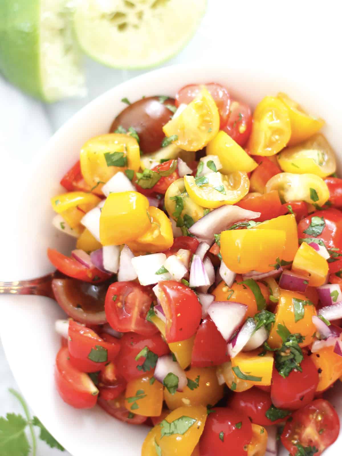 Chopped cherry tomatoes in a bowl mixed with red onion and cilantro.