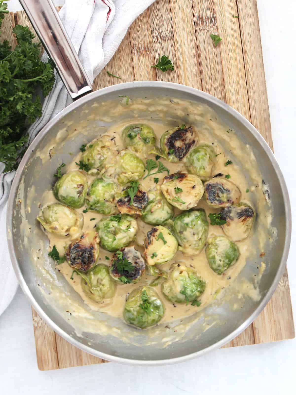 Creamed Brussels sprouts in a skillet on a wooden chopping board.