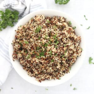 A bowl of tricolor quinoa garnished with fresh parsley.