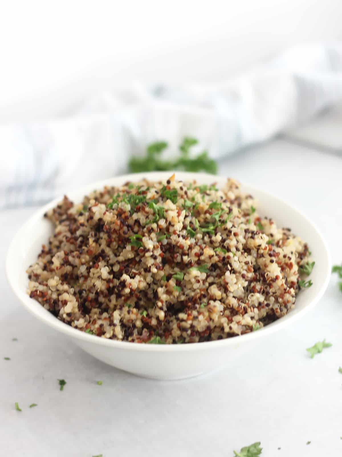 A bowl of tri-color quinoa next to fresh parsley sprigs.