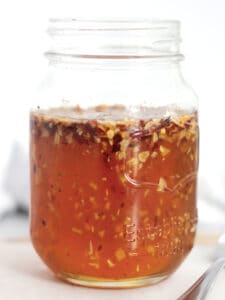 Chili flakes and minced garlic floating in honey in a jar.