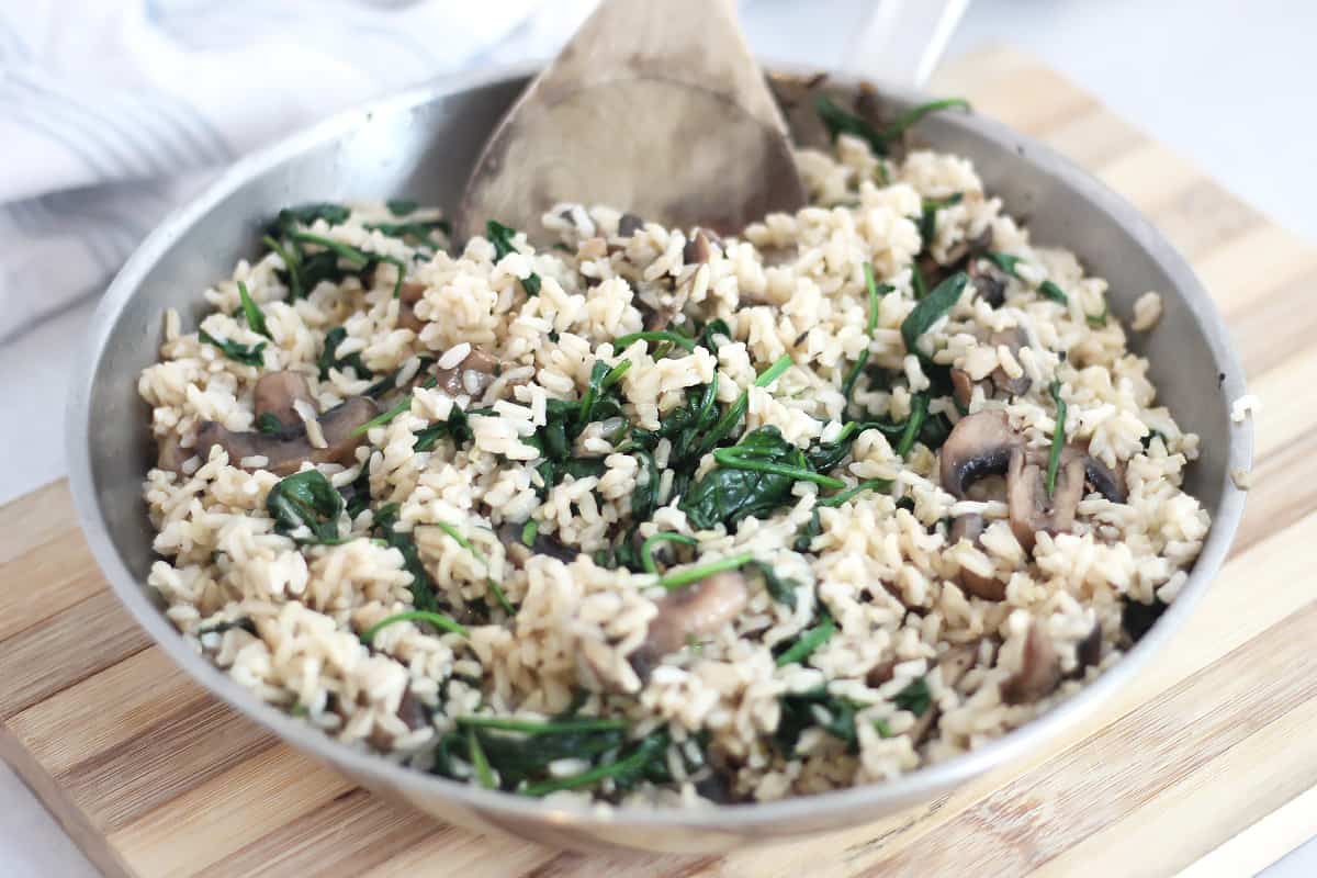 Rice with mushroom and spinach in a skillet with a wooden spoon.