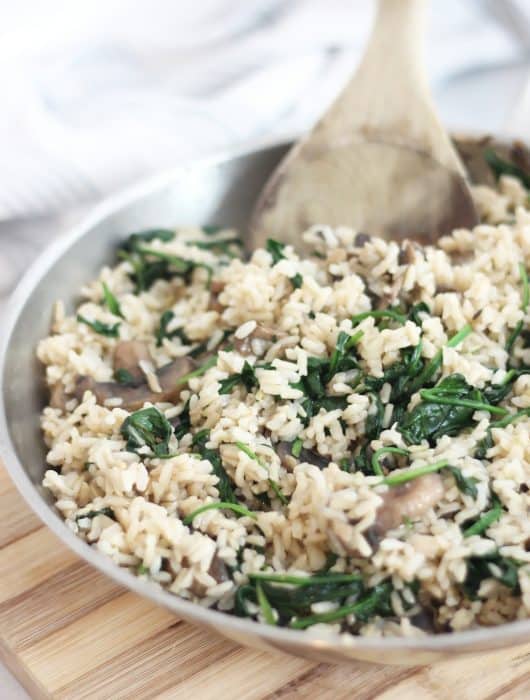 Close up of mushroom spinach rice in a skillet on a wooden chopping board.