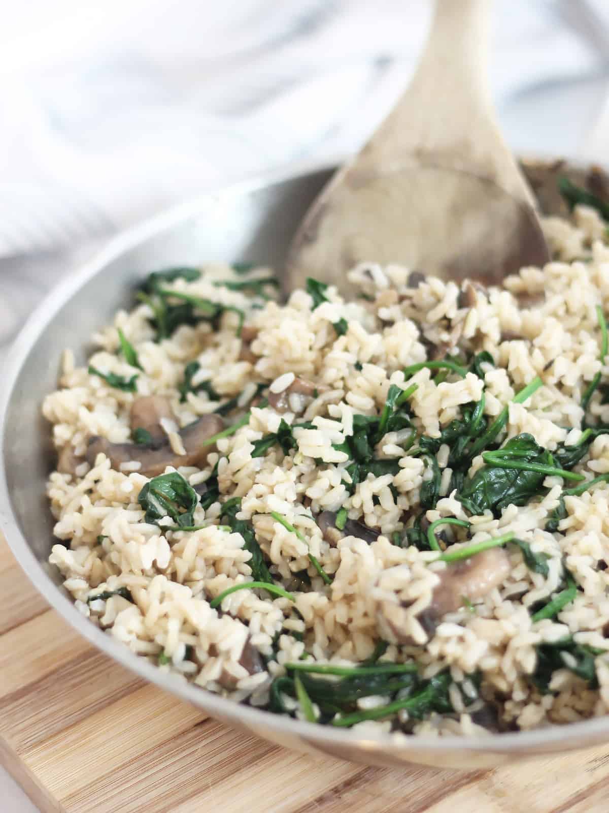 Close up of mushroom spinach rice in a skillet on a wooden chopping board.