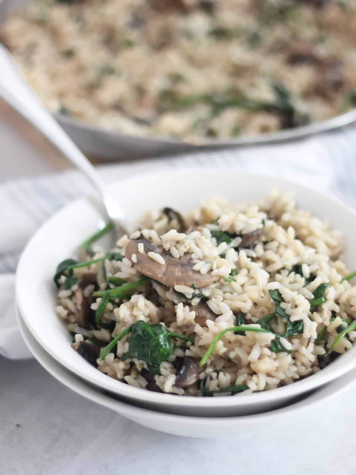 Spinach mushroom rice in a white bowl with a spoon.