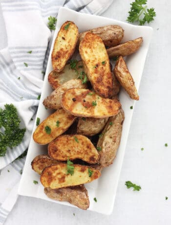 Golden air fried fingerling potatoes on a plate with fresh parsley.