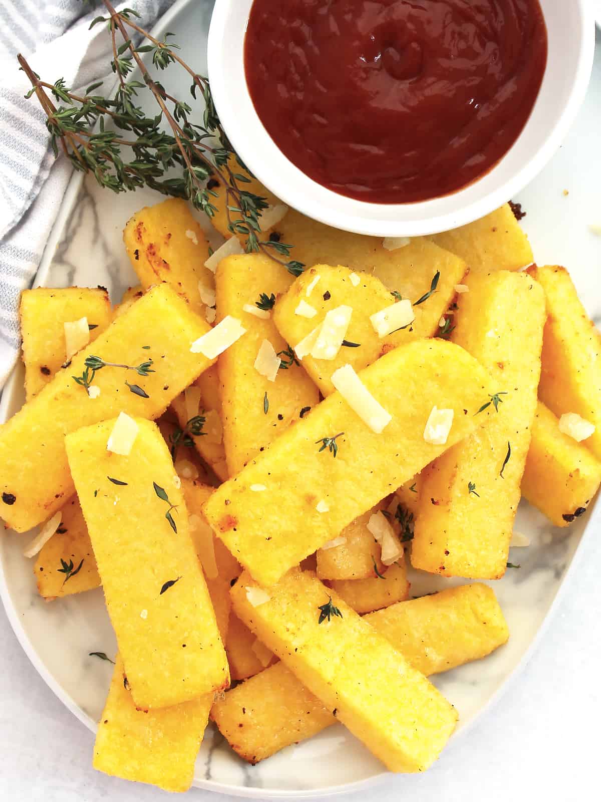 Polenta fries served on a plate with a bowl of tomato ketchup.