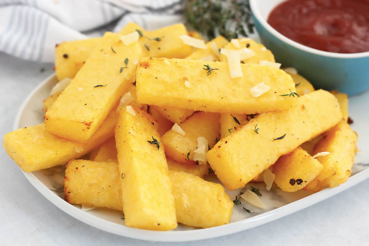 Polenta fries garnished with grated parmesan and fresh thyme sprigs.