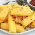 Air fryer polenta fries garnished with parmesan and fresh thyme.