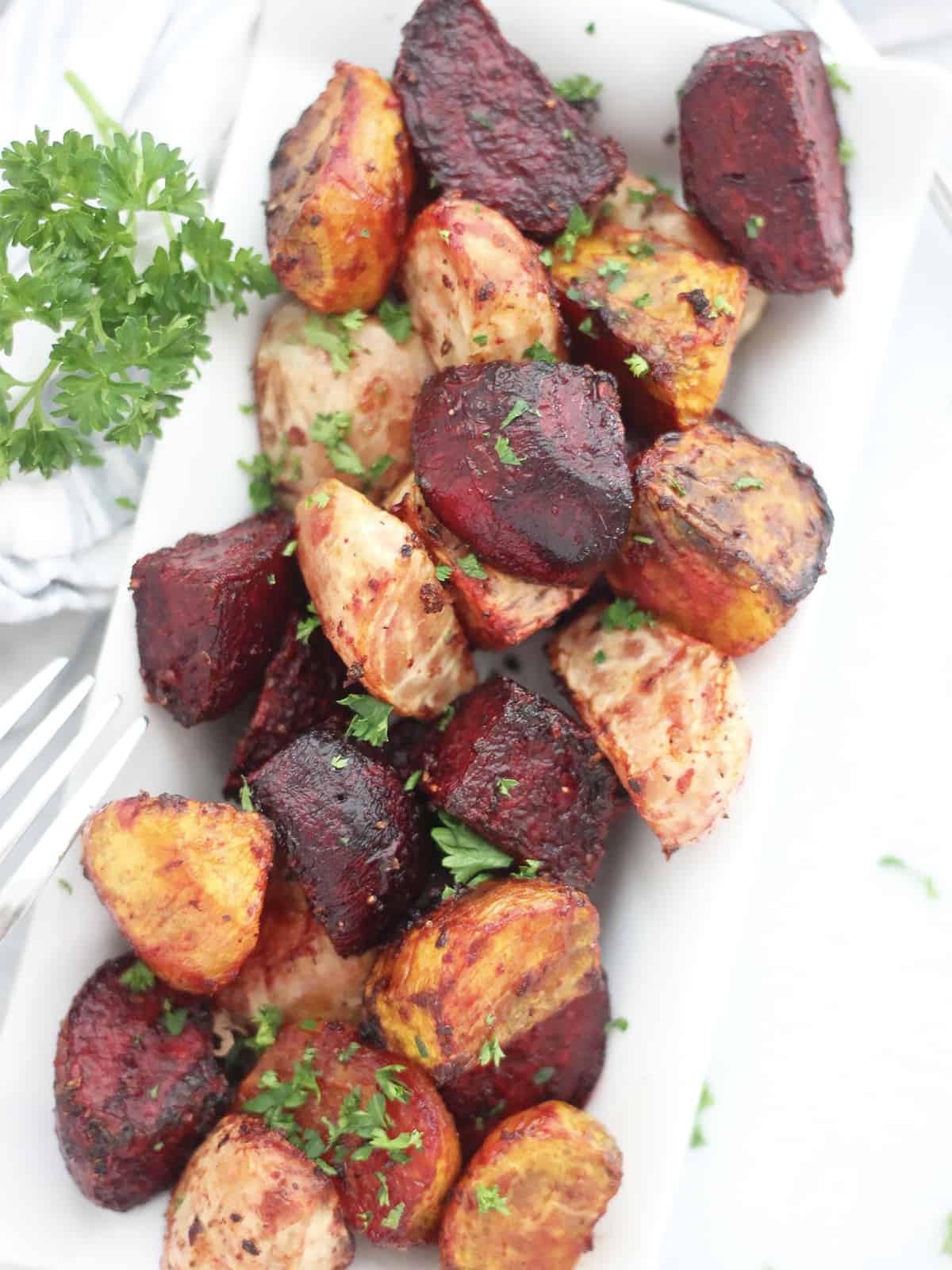 Overhead shot of air fryer roasted beetroots on a white plate with fresh parsley garnish.