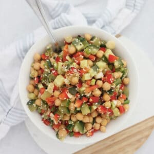 Chickpea, cucumber and red pepper salad in a white bowl with a spoon.
