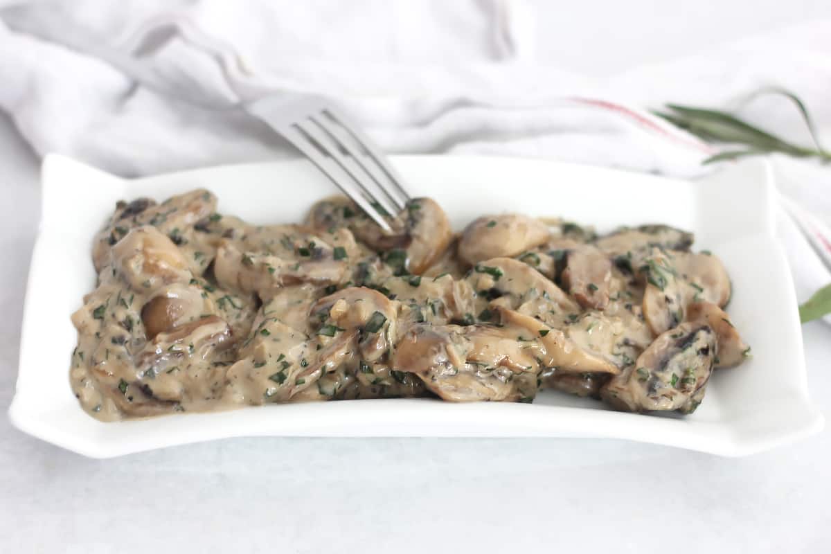 Creamy tarragon mushrooms served on a white plate with a fork.