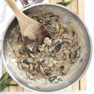 Tarragon mushrooms and cream in a skillet with a wooden spoon.