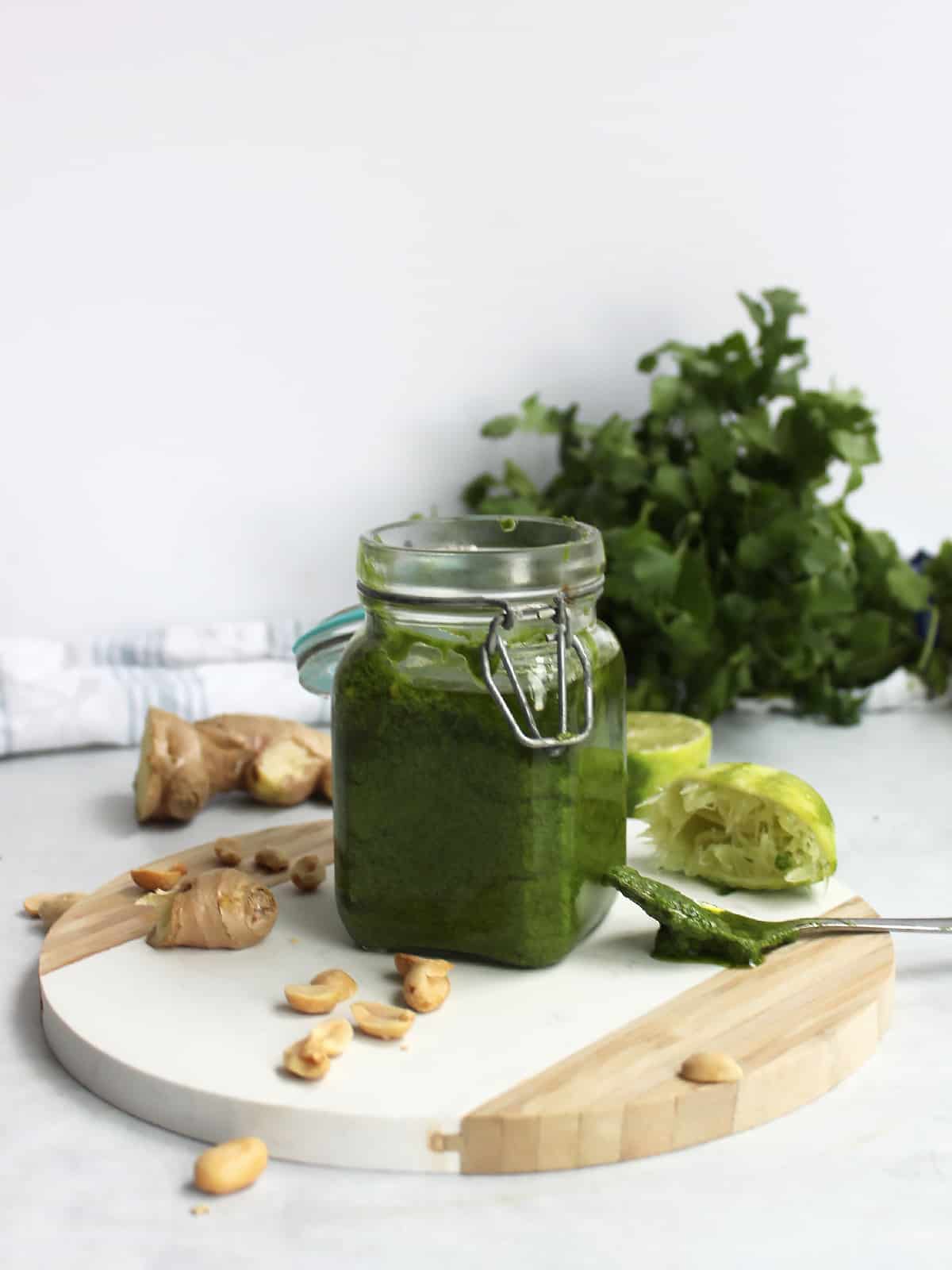 A jar of pesto on a wooden chopping board surrounded by the ingredients used to make it.