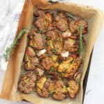 Smashed fingerlings on a baking sheet with sprigs of fresh rosemary.