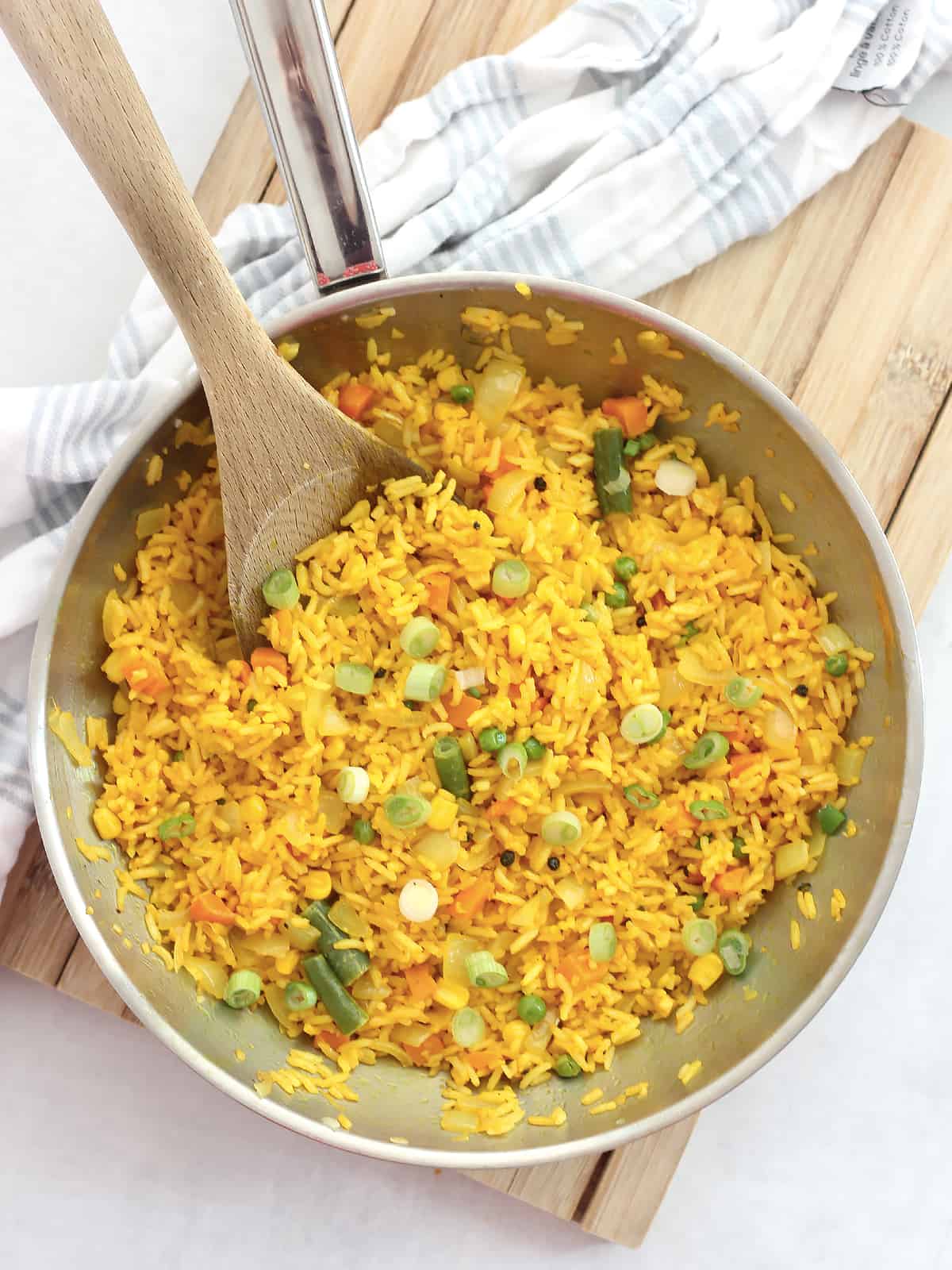 Overhead shot of turmeric fried rice in a skillet with a wooden spoon.