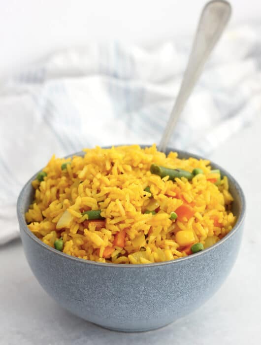 Golden fried rice and vegetables in a bowl with a spoon.