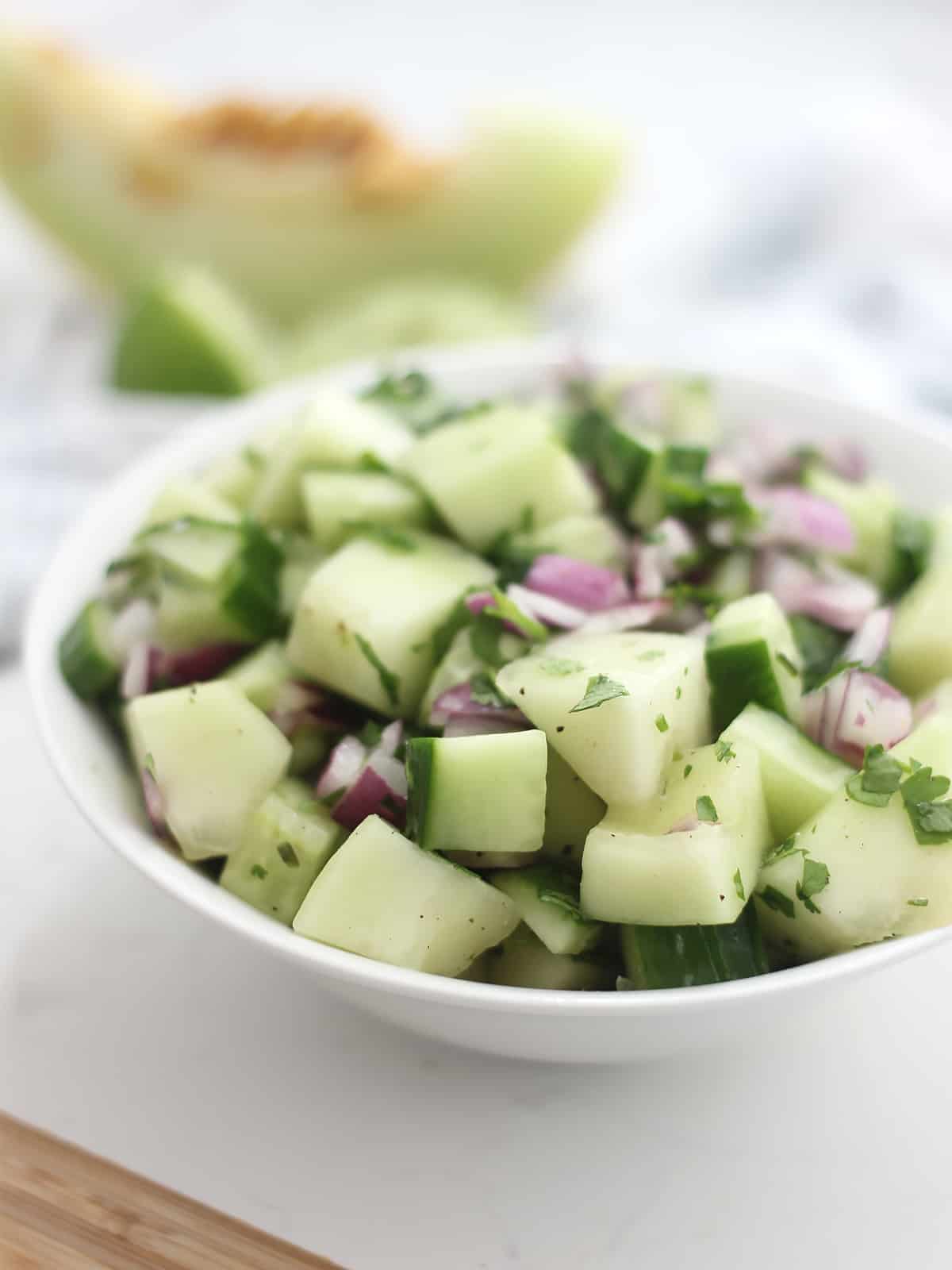 Cucumber red onion salad in a bowl in front of a slice of melon.
