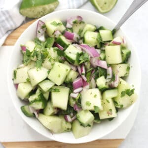 Melon and cucumber salad with red onion in a white bowl with a spoon.