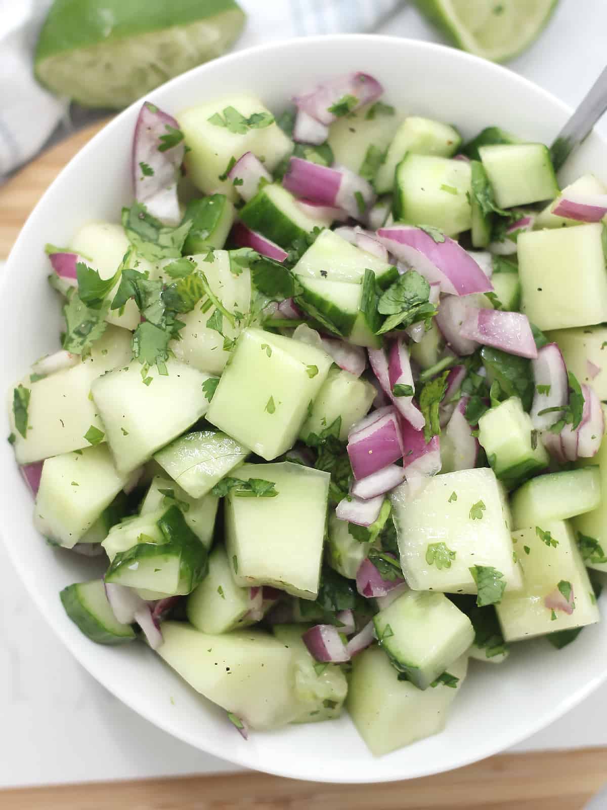 Chunks of melon and cucumber in a bowl mixed with red onion and cilantro.