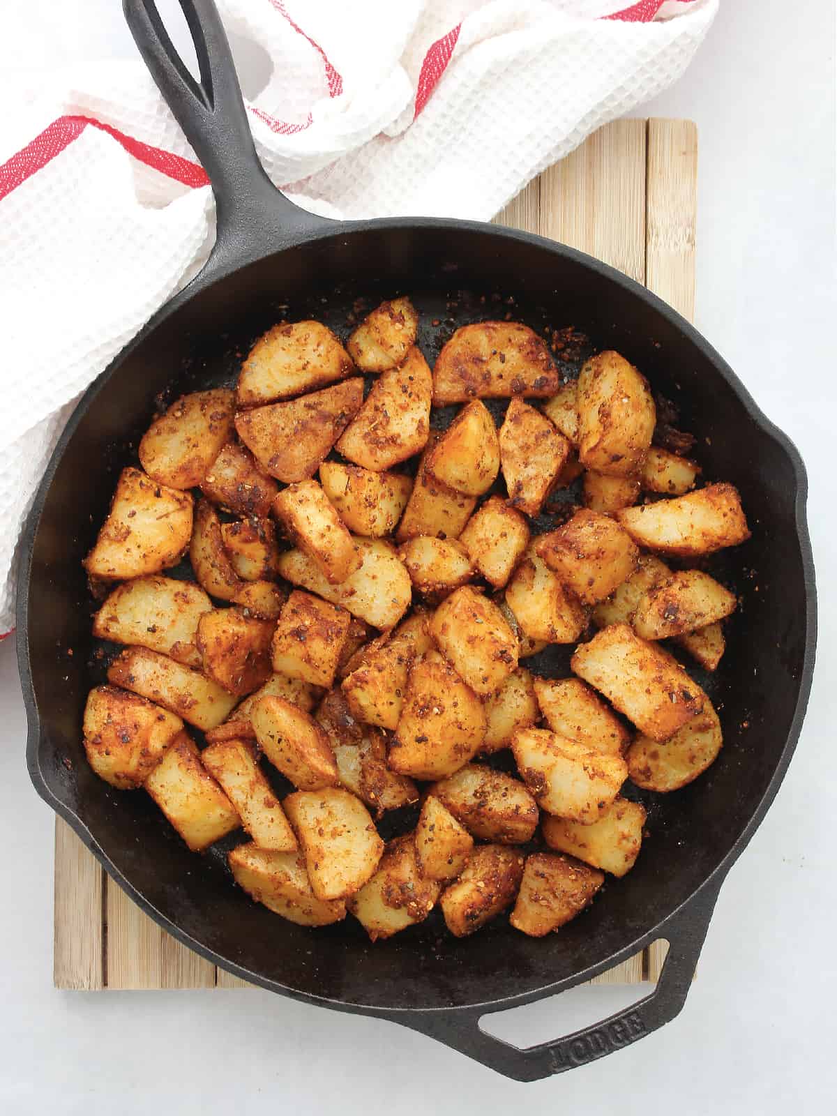 Roasted piri piri potatoes in a cast iron skillet on a wooden chopping board.