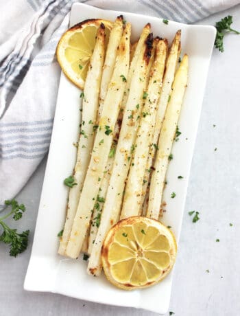 Overhead shot of roasted white asparagus spears on a serving plate with slices of lemon.