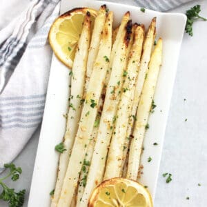 Roasted white asparagus spears served with lemon slices on a white plate.