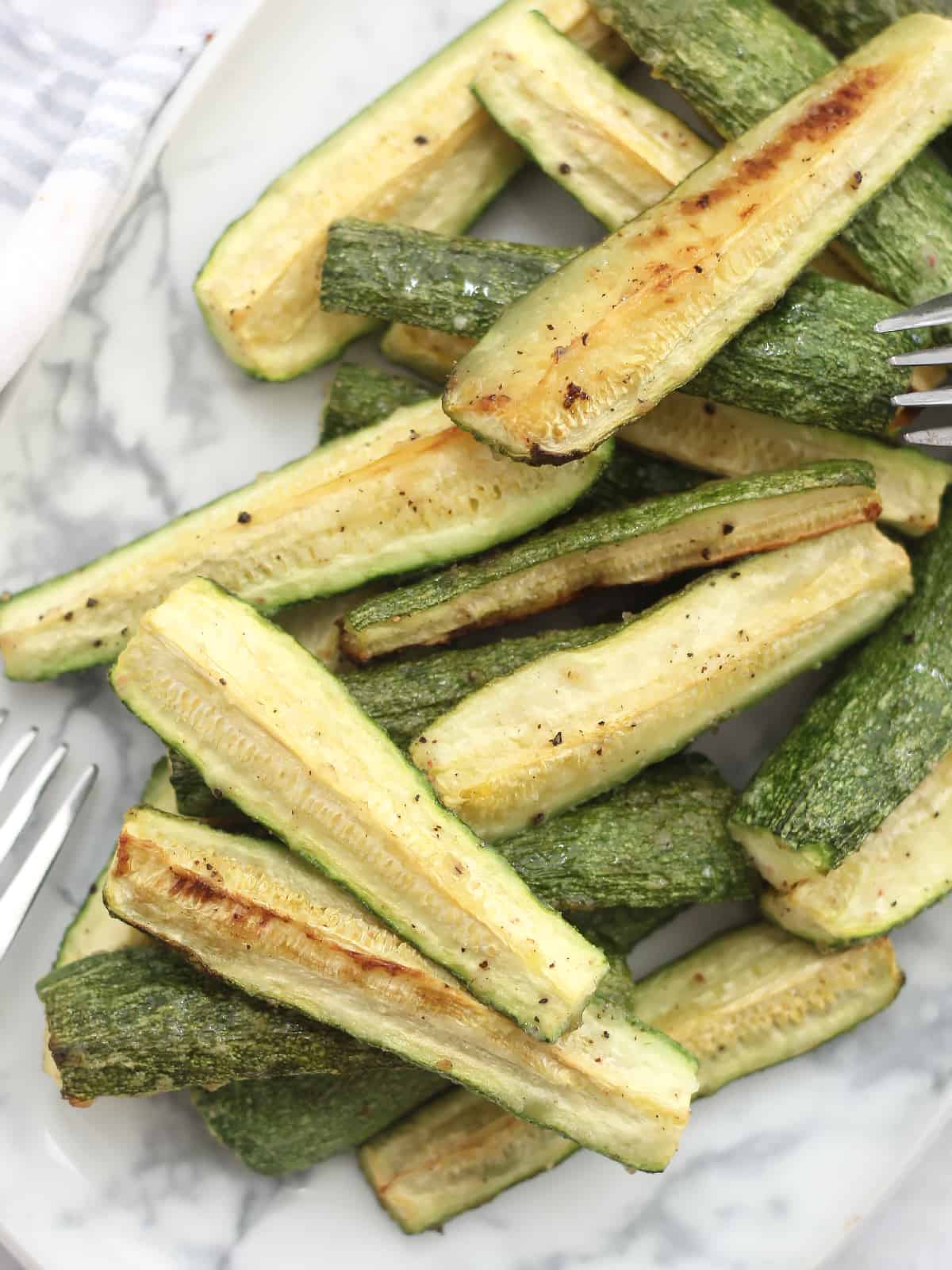 Roasted zucchini spears piled on to a serving plate.