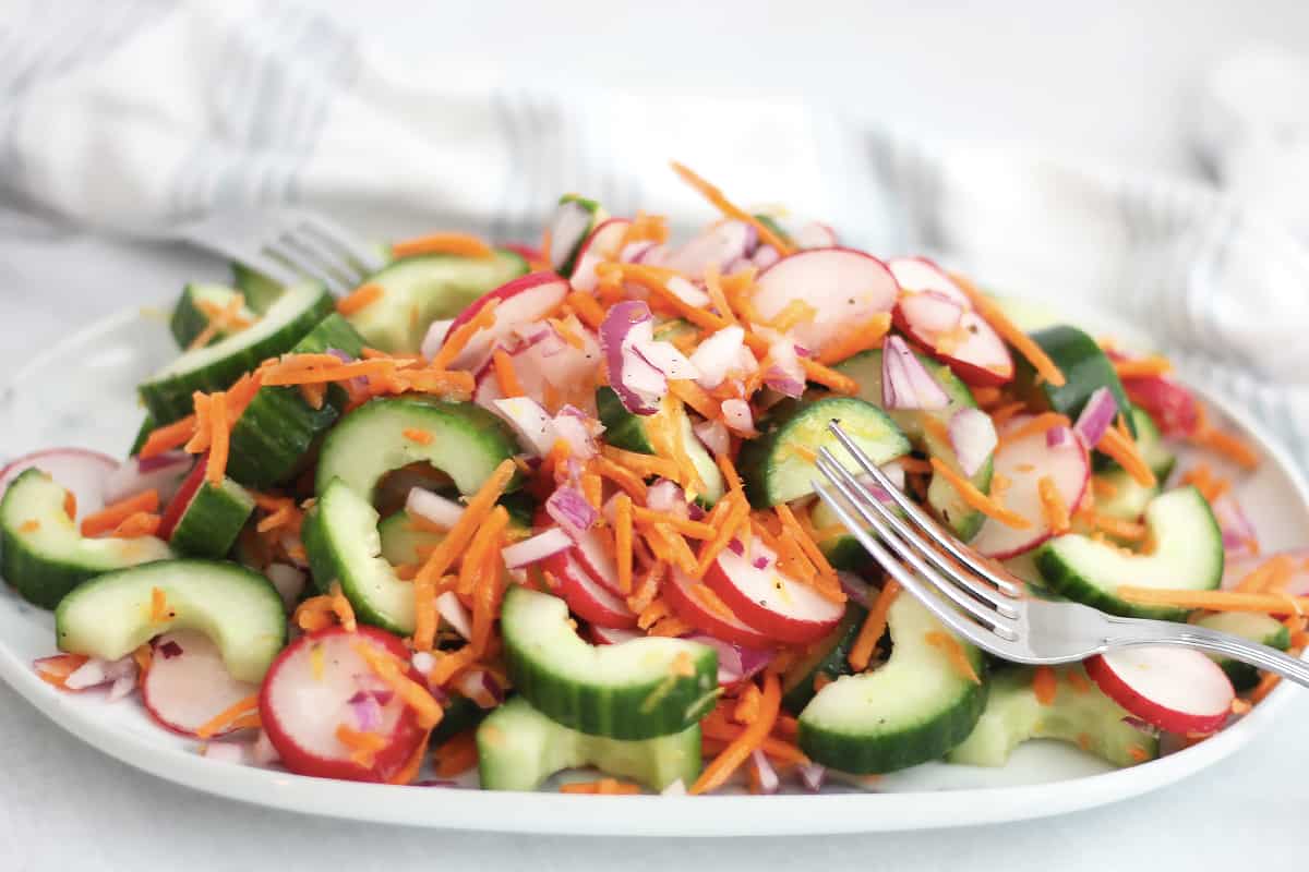 Carrot cucumber and radish salad on a plate with two forks.