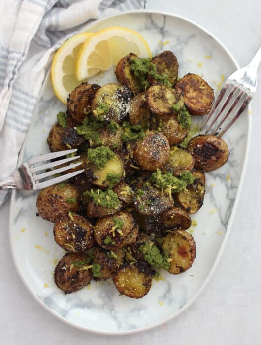 Overhead shot of roasted pesto baby potatoes on a plate with lemon slices and two forks.