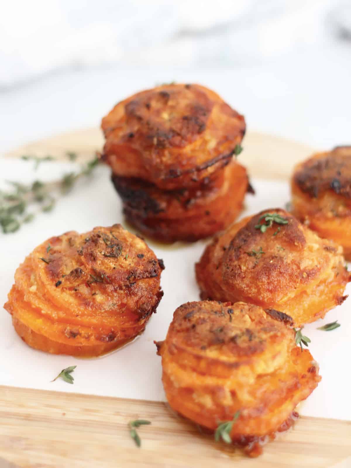 Five sweet potato stacks on a chopping board with fresh thyme.