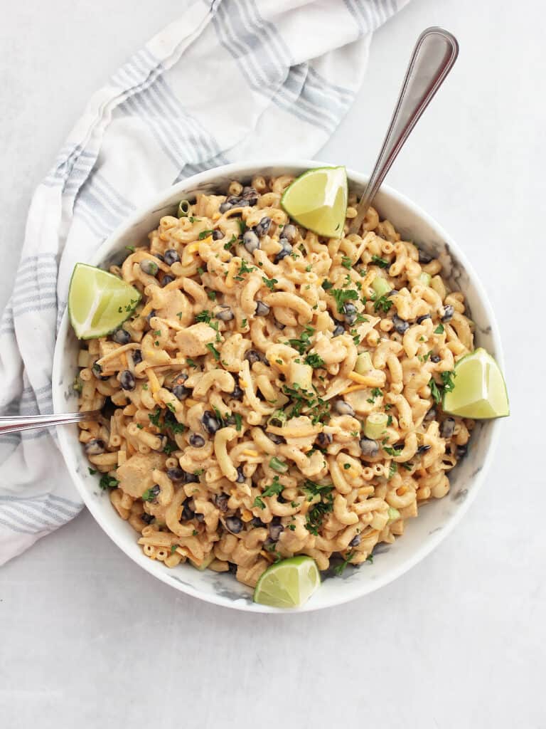 Overhead shot of a creamy taco pasta salad in a serving bowl garnished with lime wedges and cilantro.