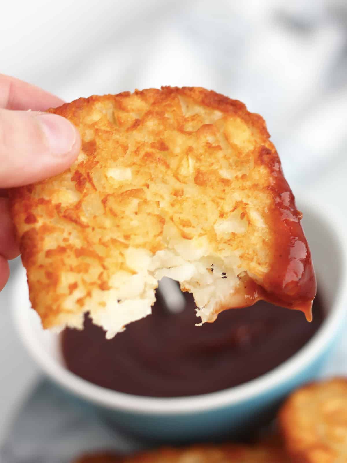 A hash brown broken in half and dipped in sauce.