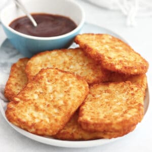 Air fried hash browns on a serving plate with a small bowl of sauce.
