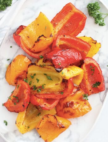 Overhead shot of yellow, red and orange air fryer roasted peppers on a plate with fresh parsley sprigs.