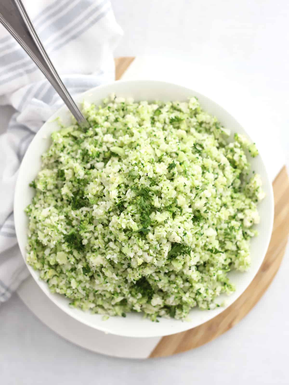 Overhead shot of broccoli cauliflower rice in a white bowl with a spoon.