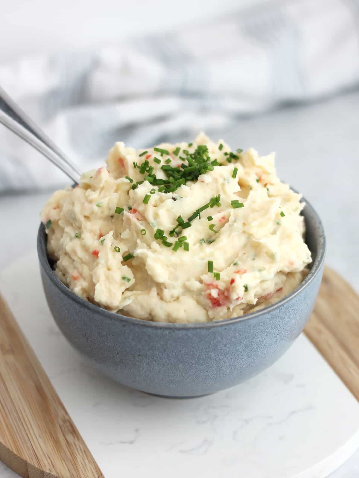 A bowl of cold mashed potato salad on a wooden chopping board.