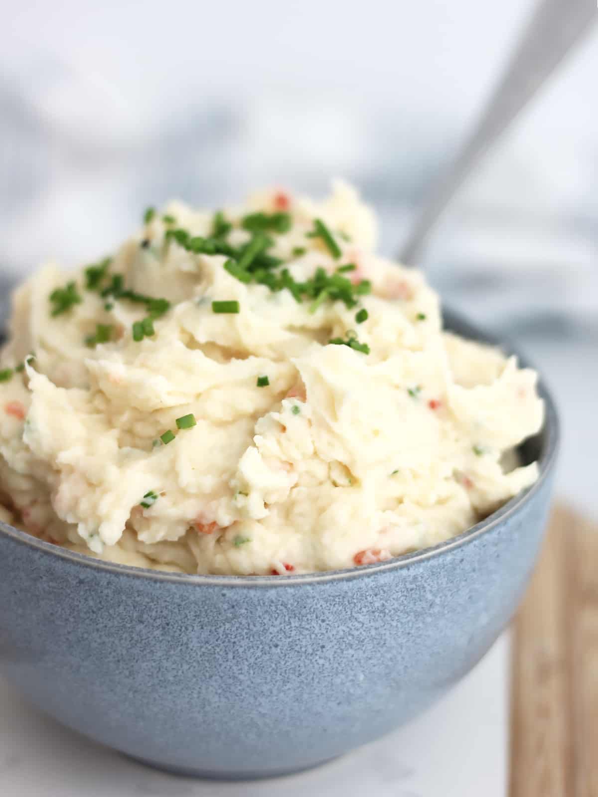 Close up of mashed potato topped with shives in a blue bowl.