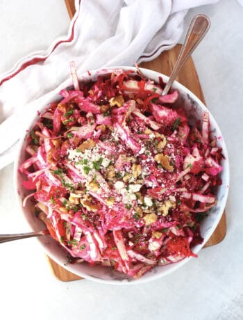Beet, cabbage and carrot slaw in a bowl topped with feta and walnuts.