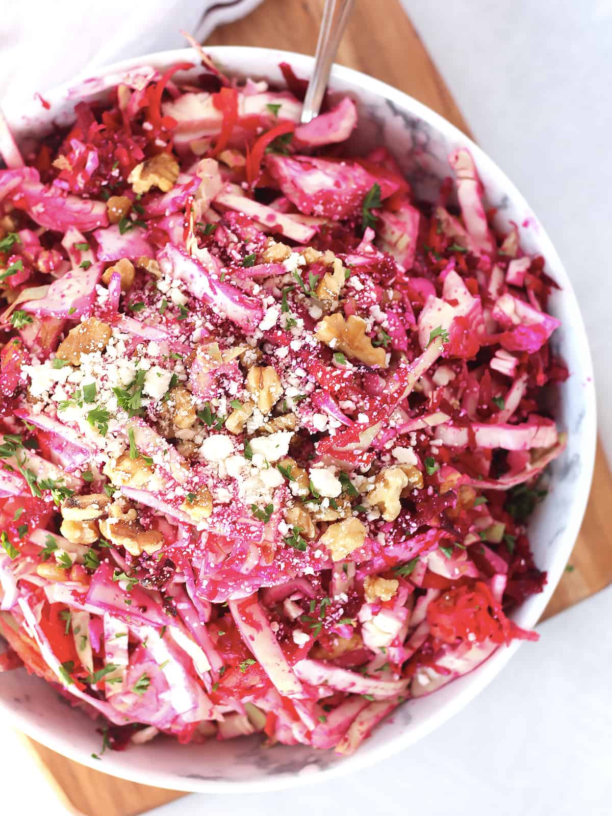 A spoon in a bowl of raw beet slaw topped with feta and walnuts.