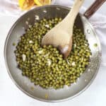Sautéed green peas in a skillet next to two freshly squeezed lemon halves.