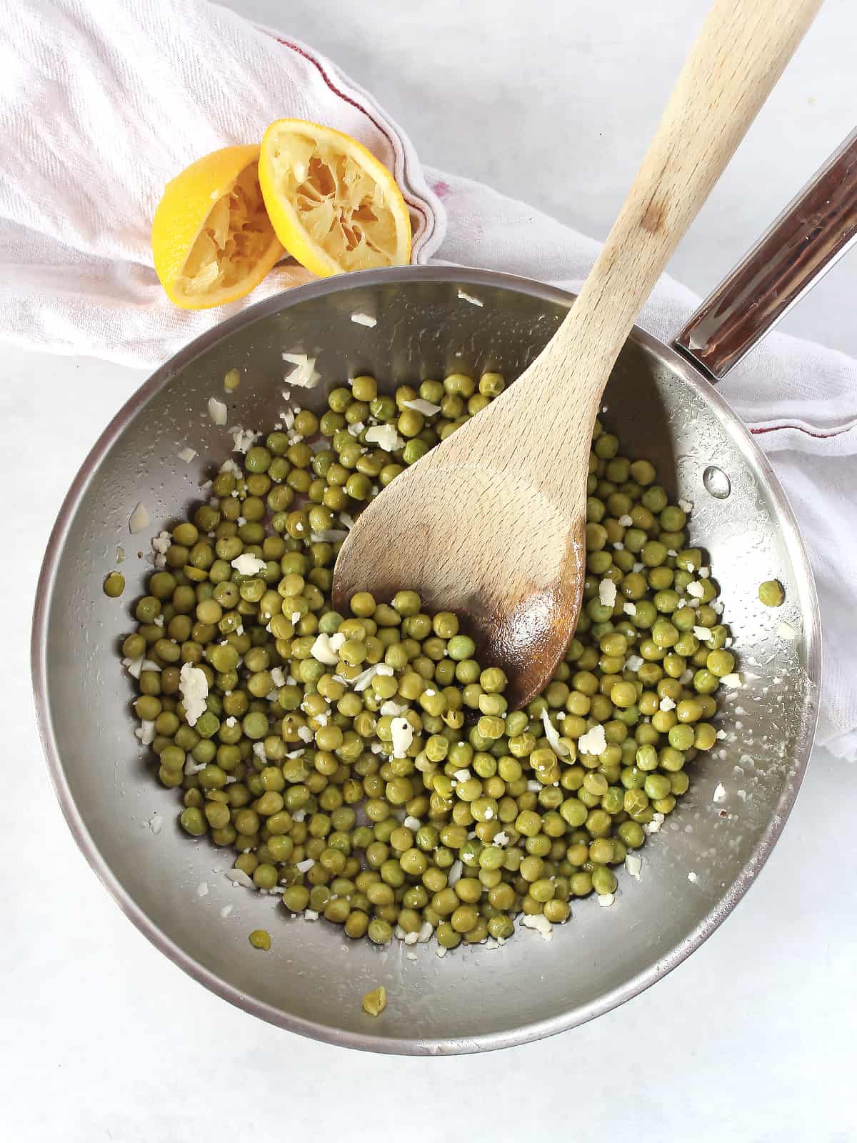 Lemon green peas in a silver skillet with a wooden spoon.