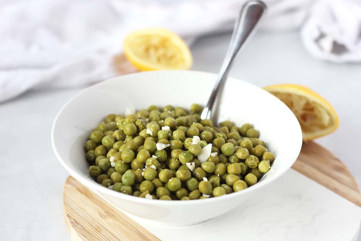 Lemon green peas in a white bowl with a spoon.
